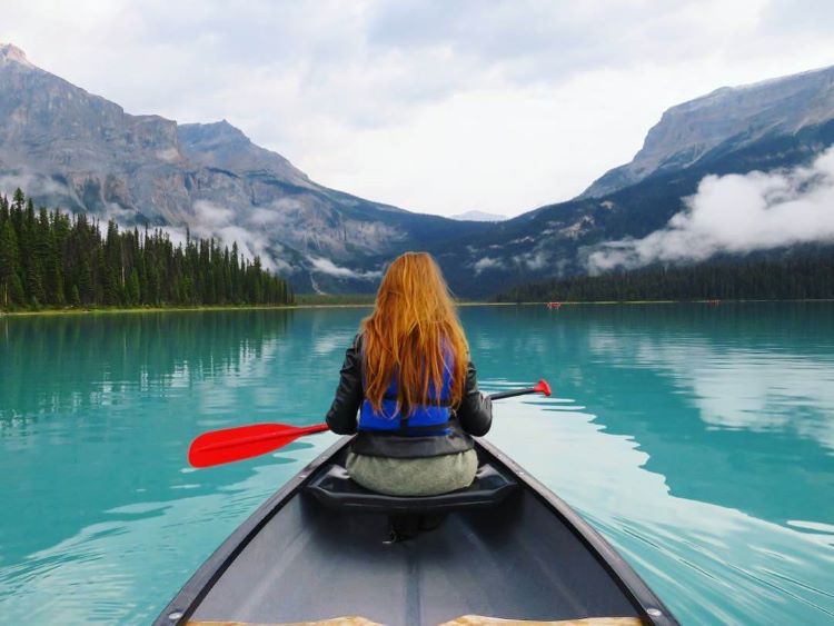 Mädchen mit roten Haaren geht auf dem blauen Smaragdsee in den kanadischen Rocky Mountains Kanu fahren. 